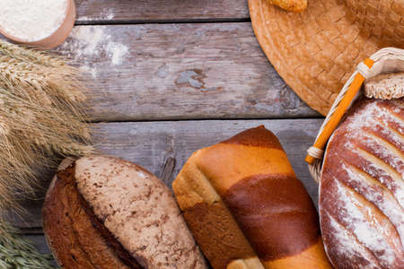 Assorted bread on wooden background. Various types of bread, wheat ears and bowl with organic flour....