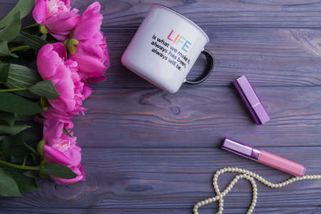 Woman's accessories on wood with copy space. Peony flowers, cup, lipstick, mascara and pearl necklace arranged around with free space.の写真素材