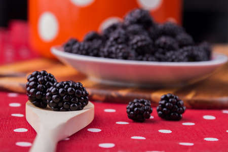 Wooden tablespoon with blackberries, close-up. Plate with berries background, cooking or eating...