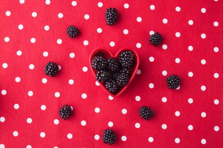 Blackberries in a heart form, flat lay. Top view, heart in a circle, red dotted background.