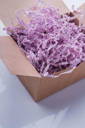 Opened cardboard box with purple decorative shredded paper. Close-up, top view.の写真素材