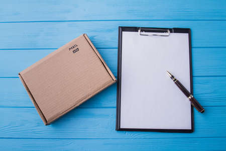Clipboard and carton cardboard box, flat lay. Top view. Blue wood background.の写真素材