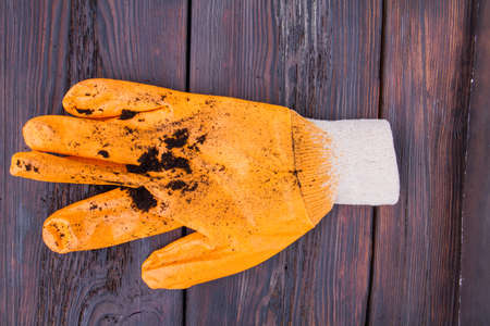 Orange garden glove with soil dirt after hard work. Fark wooden background.の写真素材