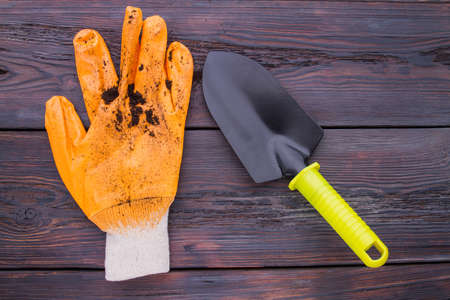 Used dirty gardening glove and trowel. Close-up. Wooden background.の写真素材