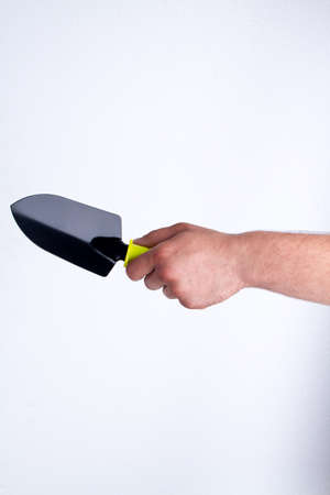 Mans hand holding gardening trowel. Black stee tool, isolated on white background.