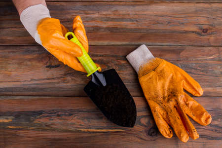 Man's hand holds garden shovel with ground. Old wood background. Top view.の写真素材