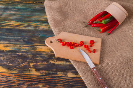 Overturned plate with peppers. Chopped chili on wooden board. Wooden background with canvas.