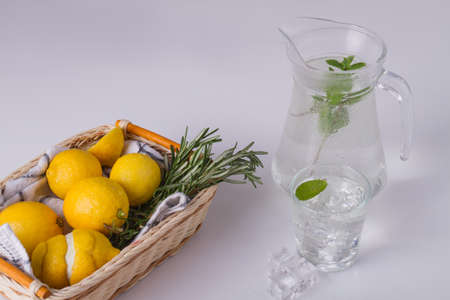 Glass cup ang jug with mint water. Lemons and rosemary sprig in basket. Food concept.