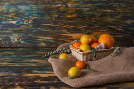 Different citruses in wicker basket on the canvas. Sage and eucalyptus leaves. Wooden background.の写真素材