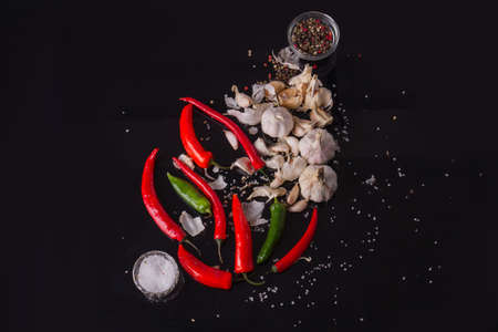 Capsicum annuum and garlic heads in focus. Allspieces and salt in glass cups. Black studio.