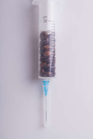 Medical syringe full of coffee beans over white background. Plastic syringe with coffee seeds. Caffeine addiction concept.の写真素材