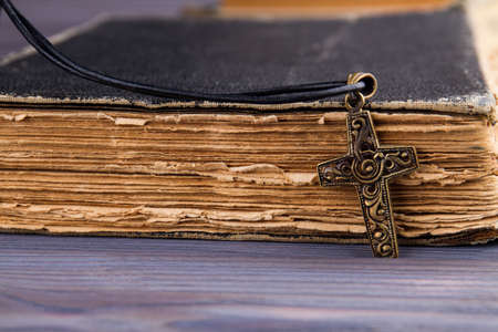 Closeup of christian cross with on holy Bible with a black cover. Very old book and copper crucifix, side view.の写真素材