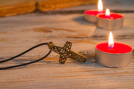Copper cross and burning candles. Christian spirituality concept.の写真素材