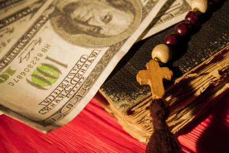 Close up old book, wooden cross on bead necklace and money. Religion and money concept.の写真素材