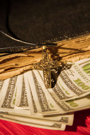 Money in book, church tethe concept. Close up, old vintage holy bible, us dollars and golden cross.