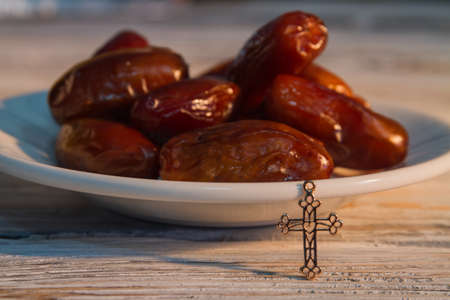 Plate of date fruits and small golden cross. Closeup. Christian holy dessert.の写真素材