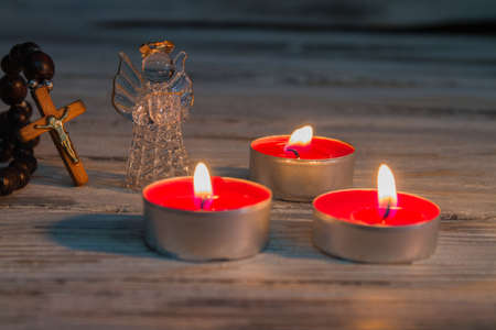 Christmas eve atmosphere concept. Glowing flat round candles, crystal glass angel and crucifix...