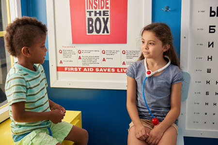 31.07.2017 - Kyiv, Ukraine. Beautiful girl playing oculist at medical office. Two little girls playing doctor and patient. Ophthalmology, eye doctors office.の写真素材