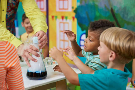 Happy kids at entertainment center. Children enjoying chemical show in playroom. Birthday party for...