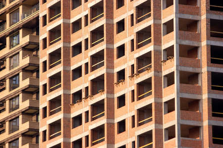 Brown high living building under construction. Facade of a multistoried house with empty windows.