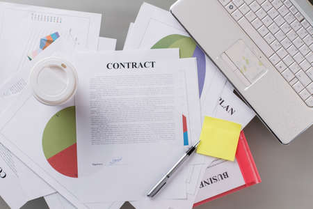 Signed contract and buisness plan. Plastic cup, pen, sticker and laptop in focus. Business affairs.の写真素材