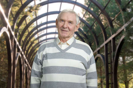 Positive old man portrait. Grandfather in striped sweater. Metal construction framework background.