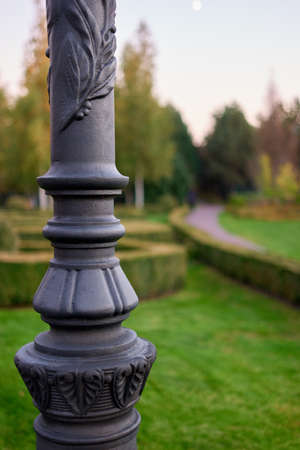 Decorative lamp post column in a park. Ornamental black metal close up.