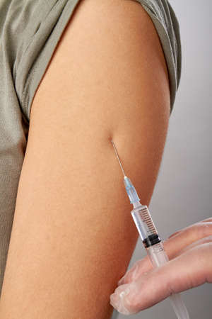 Vaccination in the shoulder of female patient. Close up syringe needle injecting into woman's arm.の写真素材