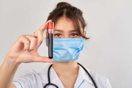 Young female doctor holding blood test tube with her fingers. Isolated on grey background.の写真素材