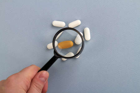 Observing pills medicines using magnifying glass. Isolated on grey background.