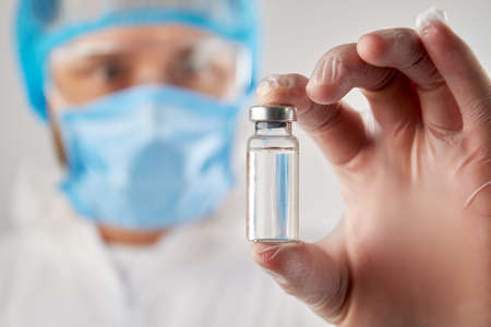 Doctors hand holding a vial of clear liquid for injection. Close up transparent bottle ampulas...