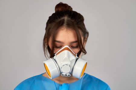 Portrait of a young woman with closed eyes wearing protective respiratory mask. Isolated on grey background.の写真素材