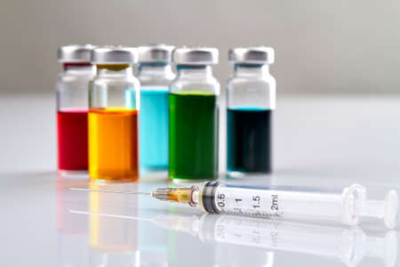 Syrynge and bottles with colored medicine. White clean reflective surface.の写真素材
