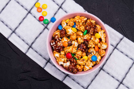 Crispy popcorn and chocolate candies mix on napkin against brown wooden background. Checkered white napkin.の写真素材