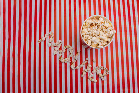 Full popcorn in bowl and popcorn arranged in movie word on red white background. Flat lay compostion...