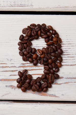 Brown roasted coffee beans arranged in a shape of nine. Seeds in a form of number nine on white...