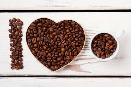 I love natural fresh coffee concept. Coffee seeds arranged in a heart shape and filling cup. White wood background.の写真素材