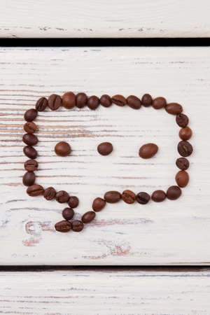 Talk bubble of coffee beans with three grains. White wood on background.