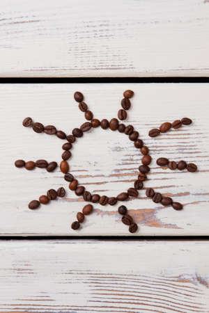 Roasted coffee beans arranged in a shape of sun. White wooden planks on background.