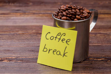 Steel mug overfilled with coffee beans. Coffee break concept. Rustic wooden background.の写真素材
