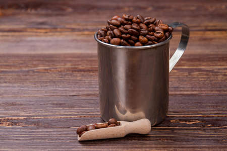 Steel mug and wooden scoop for coffee beans. Reflective metal cup on brown wood.の写真素材