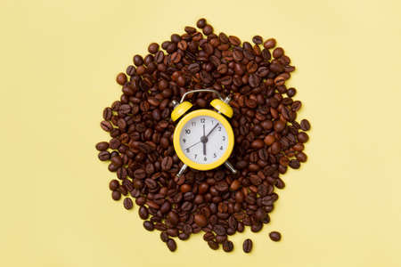 Alarm clock on a pile of coffee. Coffee time concept. Yellow background.の写真素材