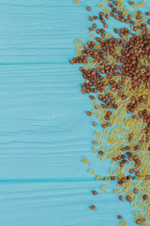 Mixed dry buckwheat and alphabet cereals on blue wood. Top view and copy space.