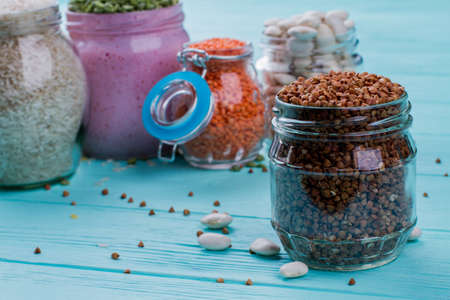 Close up glass transparent can of buckwheat. Fresh raw grains for canning. Blue wooden surface.の写真素材