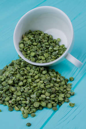 Heap of green split peas out of a cup. Blue wood background.の写真素材