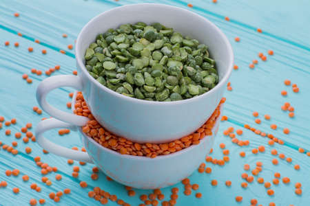 Close up cereals in a white cups. Scattered orange grains on a blue wooden background.