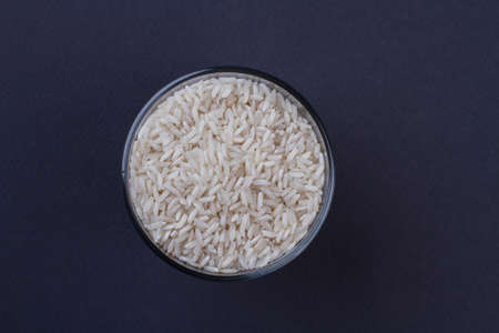 Top view uncooked raw rice in a transparent glass cup. Dark blue background.の写真素材