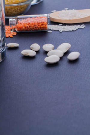 Close up bunch of white beans on blue table with copy space. Mini bottle with dry lentils.