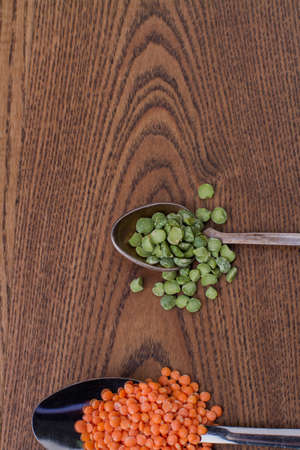 Teaspoon with bunch of green split peas. Tablespoon with lentils groats. Brown wooden background.の写真素材
