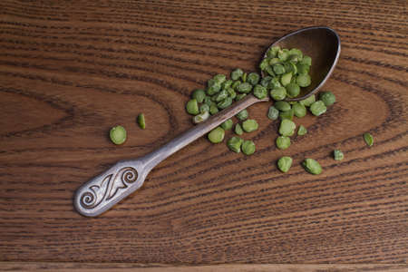 Close up teaspoon with green split peas grains on wood. Raw uncooked fresh cereals.の写真素材